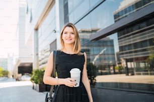 테이크아웃 커피를 마시면서 일하러 걸어가는 젊은 비즈니스 여성의 초상화. 비즈니스 및 성공 개념입니다.