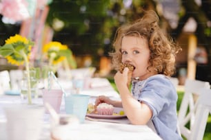 夏の庭で屋外に座っておやつを食べている小さな女の子。お祝いのコンセプト。
