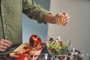 Cropped photo of a Caucasian male cook adding the lemon juice to a glass bowl