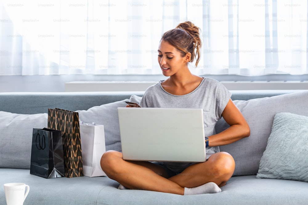 Mujer joven sosteniendo una tarjeta de crédito y usando una computadora portátil. Concepto de compra en línea. Mujer feliz haciendo compras en línea en casa