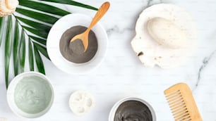 Top view SPA natural organic cosmetics and accessories on marble background with tropical palm leaf. Flat lay face clay masks, homemade soap, loofah sponge, hair comb. Face and body skin care concept