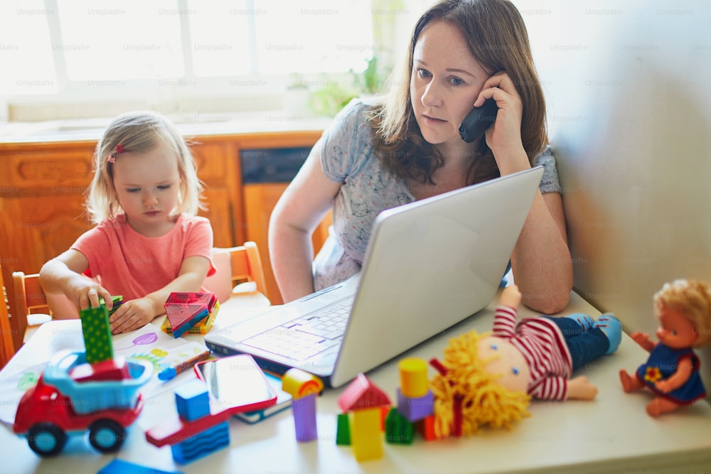 Exhausted and stressed mother working from home with toddler. Quarantine and closed daycare centres during coronavirus outbreak. Child making noise and disturbing woman at work. Freelance job with kid