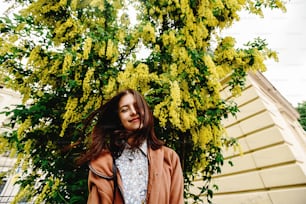 femme de luxe heureuse élégante s’amusant sous un buisson fleuri étonnant avec des fleurs jaunes, concept de bonheur