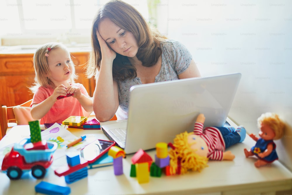 Exhausted and stressed mother working from home with toddler. Quarantine and closed daycare centres during coronavirus outbreak. Child making noise and disturbing woman at work. Freelance job with kid