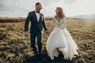 happy wedding couple walking in sunlight, holding hands in mountains at sunset light. gorgeous boho newlyweds, stylish bride and groom, true feelings. emotional romantic moment. space for text