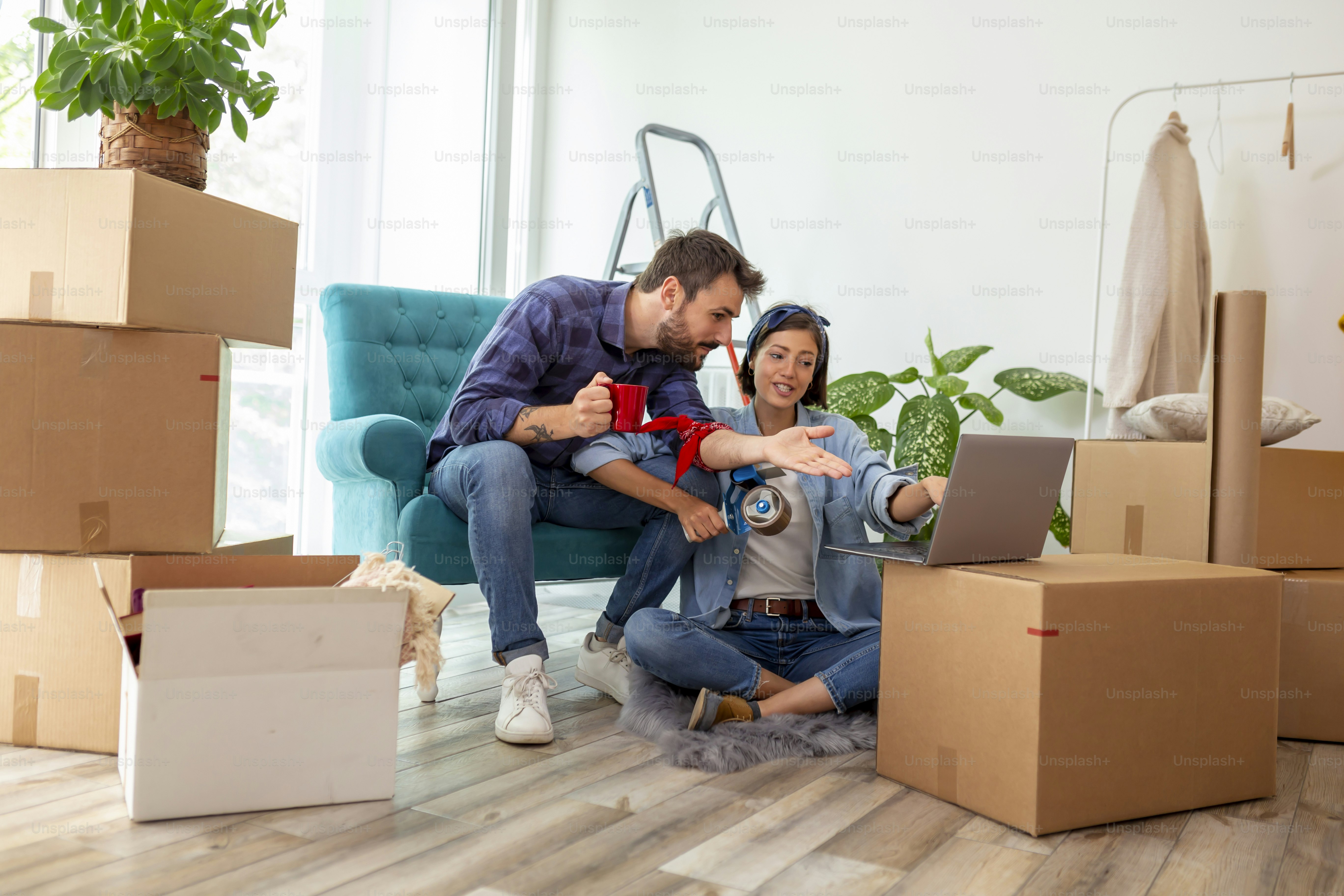 Bella giovane coppia innamorata che si trasferisce insieme, navigando in rete sul computer portatile, cercando sul web idee per la ristrutturazione dell'appartamento