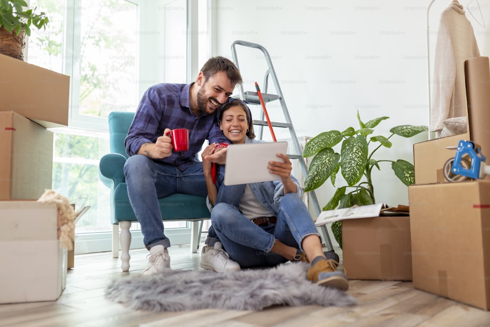 Couple in love drinking coffee and having fun while searching for home redecoration ideas using tablet computer and magazines