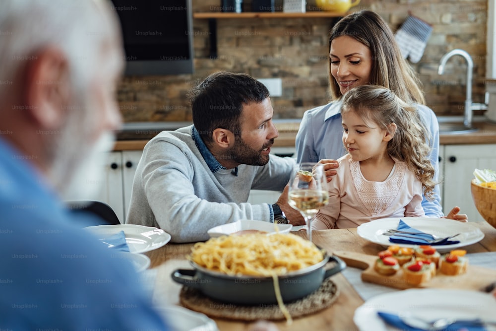 Young parents talking with their small daughter while having a meal in dining room.