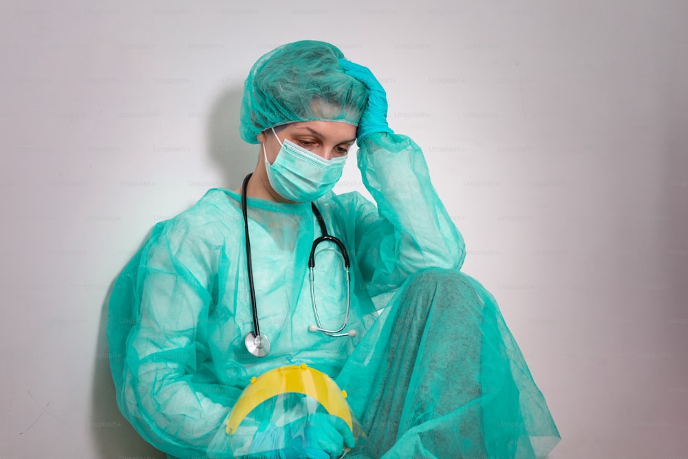 Coronavirus concept. COVID-19. Young female doctor in protective suit uniform, face mask and rubber gloves, before patient examination feeling exhausted and worried. Doctors are heroes.