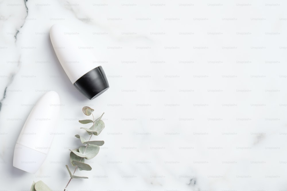 대리석 배경에 유칼립투스 잎이 있는 데오도란트 병. 플랫 레이, 평면도. 백색 발한 억제제 포장, 땀 방지 제품 개념