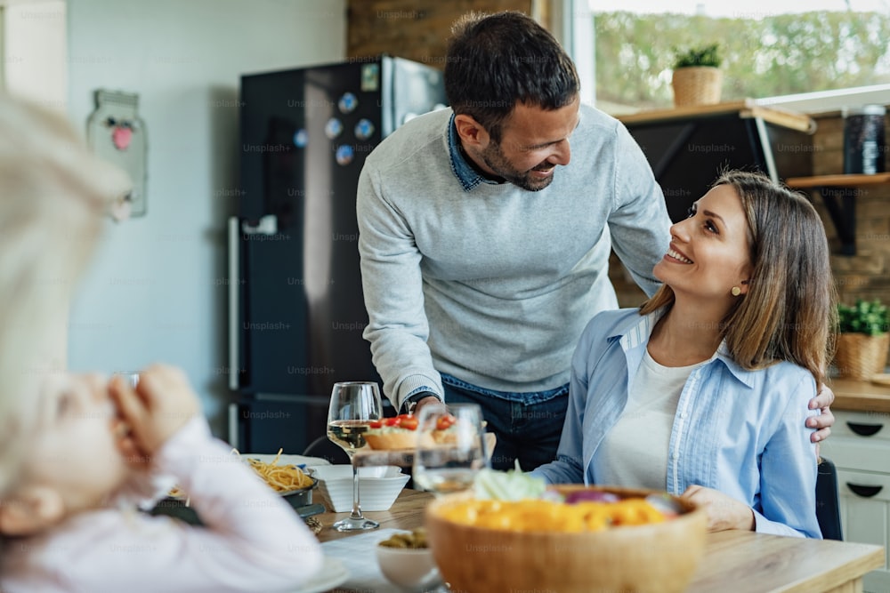 Glücklicher Mann, der Essen serviert und mit seiner Frau spricht, während er mit der Familie am Esstisch zu Mittag isst.