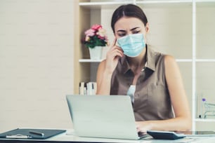 Quarantined woman working at home wearing face mask protect from Coronavirus. Concept of social distancing to stop spreading of Coronavirus Disease or COVID-19.