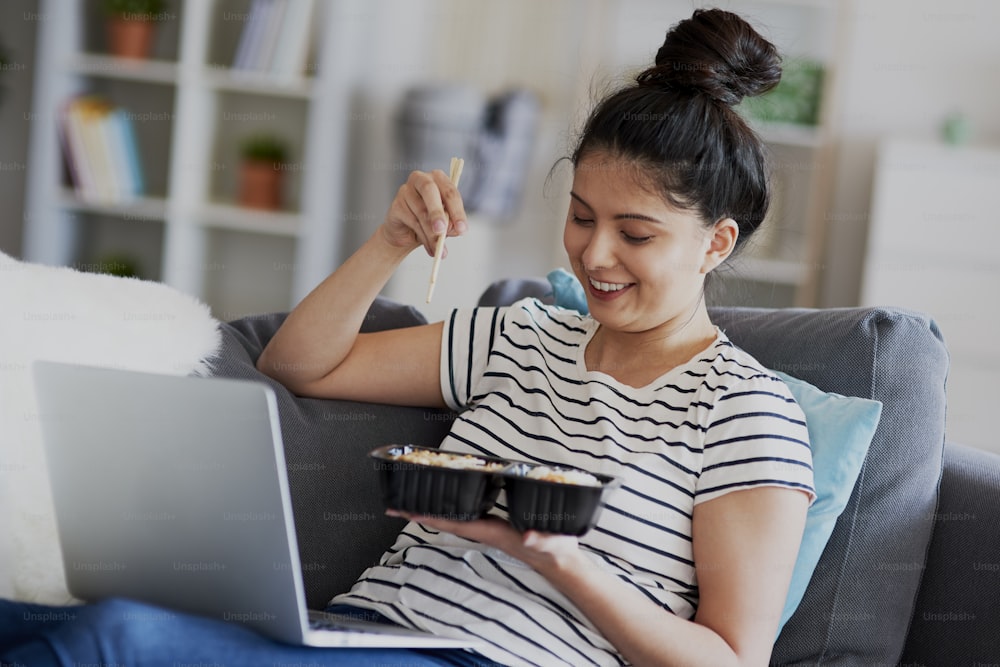 Young Asian woman eat lunch and watching something on laptop.