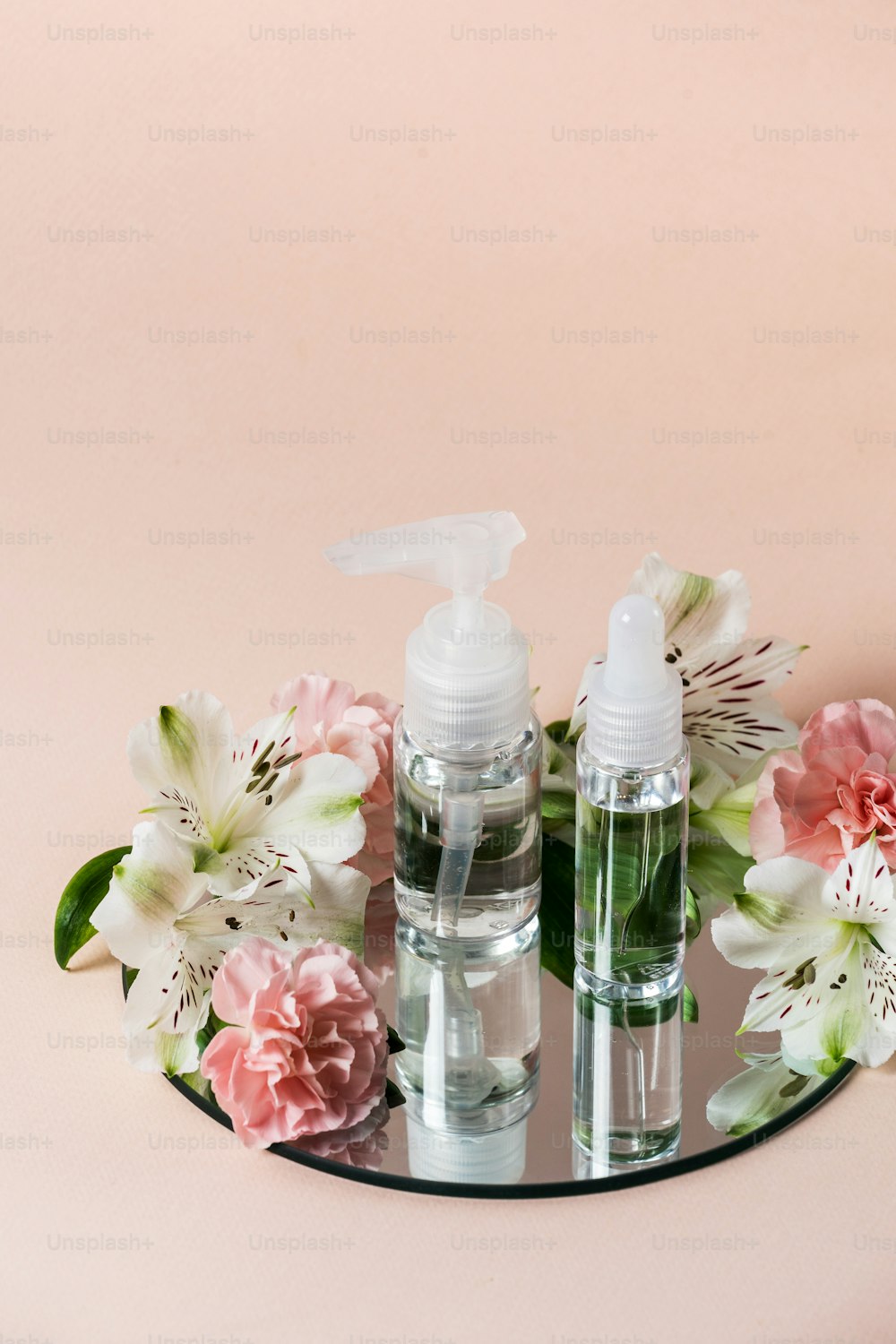 Concept of organic cosmetics product. Vertical view of transparent bottles on mirror near flowers isolated on pastel pink background with copy space