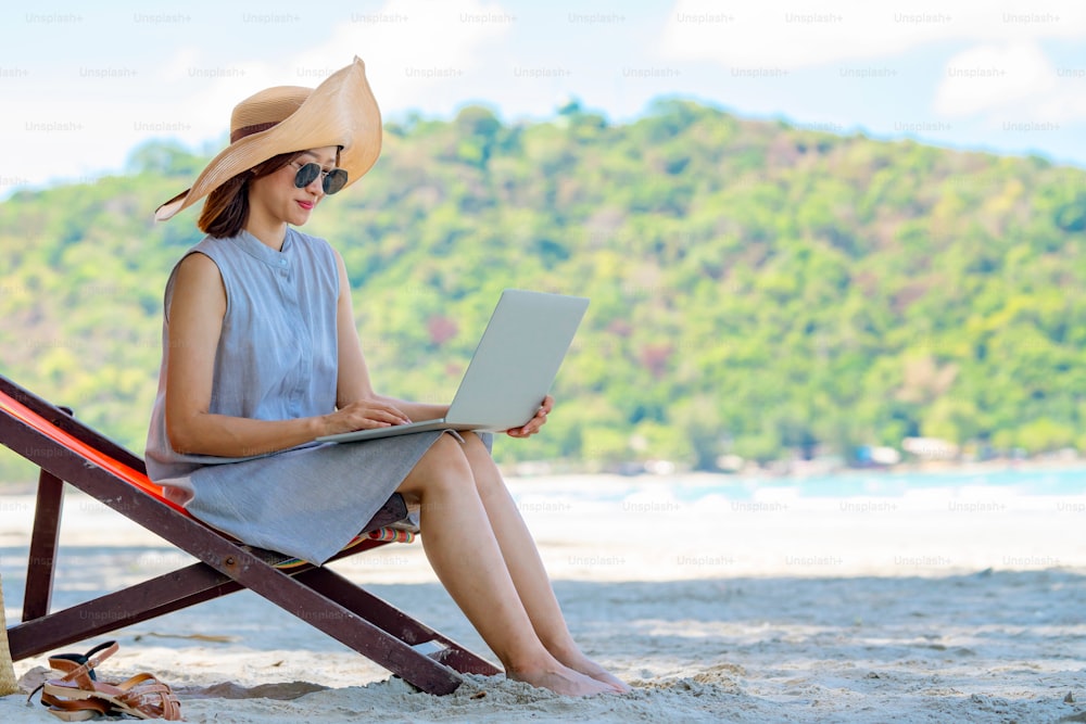 Young Asian woman sitting on beach chair with using laptop computer on the beach