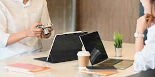 Squadra di graphic designer del primo piano che lavora insieme al computer portatile e al tablet alla scrivania di lavoro in legno sopra un comodo salotto come sfondo.