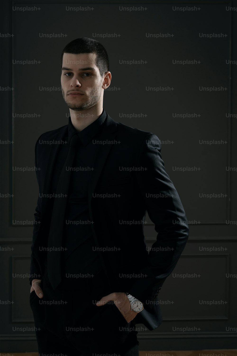 Young handsome businessman in black shirt and black suit. Confident young businessman posing on gray background