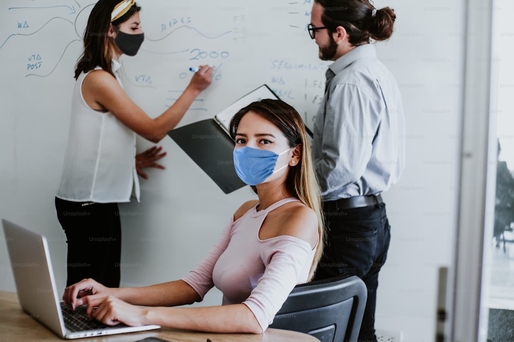 Latin woman working in business office  wearing face mask for social distancing in new normal situation protecting the infection of corona virus or covid-19, mexican coworkers in Mexico city