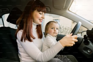 Madre con una niña sentada en el asiento delantero y conduciendo el automóvil juntas. Niño en peligro, sin seguridad en la carretera.