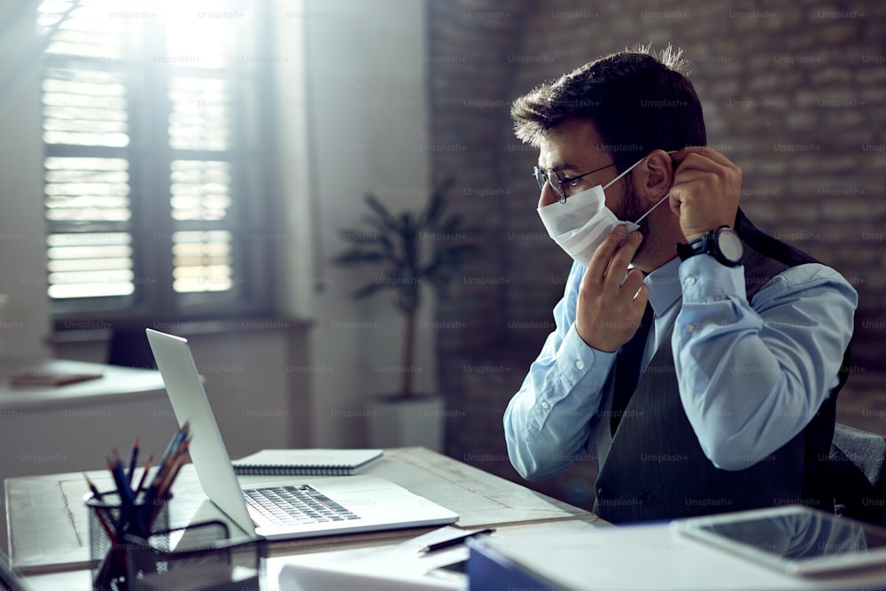 Geschäftsmann schützt sich mit einer Gesichtsmaske, während er sich auf die Arbeit im Büro vorbereitet.