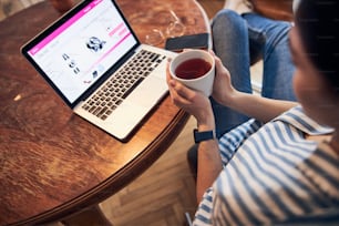 Cropped photo of woman drinking warm tea at home stock photo. Modern technology concept