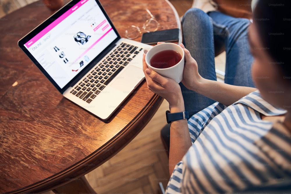 Cropped photo of woman drinking warm tea at home stock photo. Modern technology concept