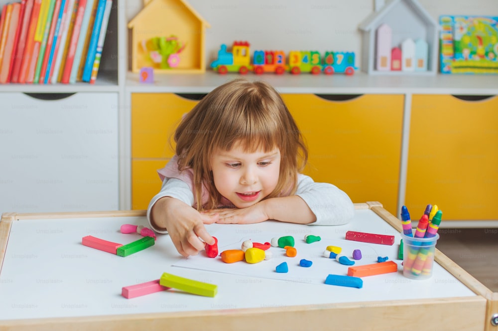 Bambina che modella gnomi colorati dall'argilla da gioco per bambini sul tavolo nella stanza dei bambini. Attività domestiche per la famiglia.