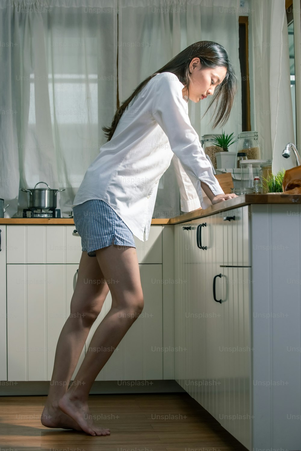 Depressed young beautiful Asian woman standing in the kitchen.