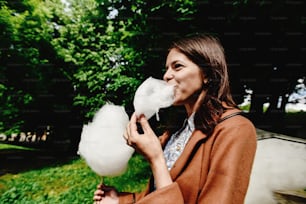 happy stylish girl holding big cotton candy and eating in amusement park in sunny spring time