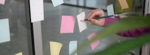 Cropped shot of businesswoman analysing on business strategy with sticky note to remind on glass wall