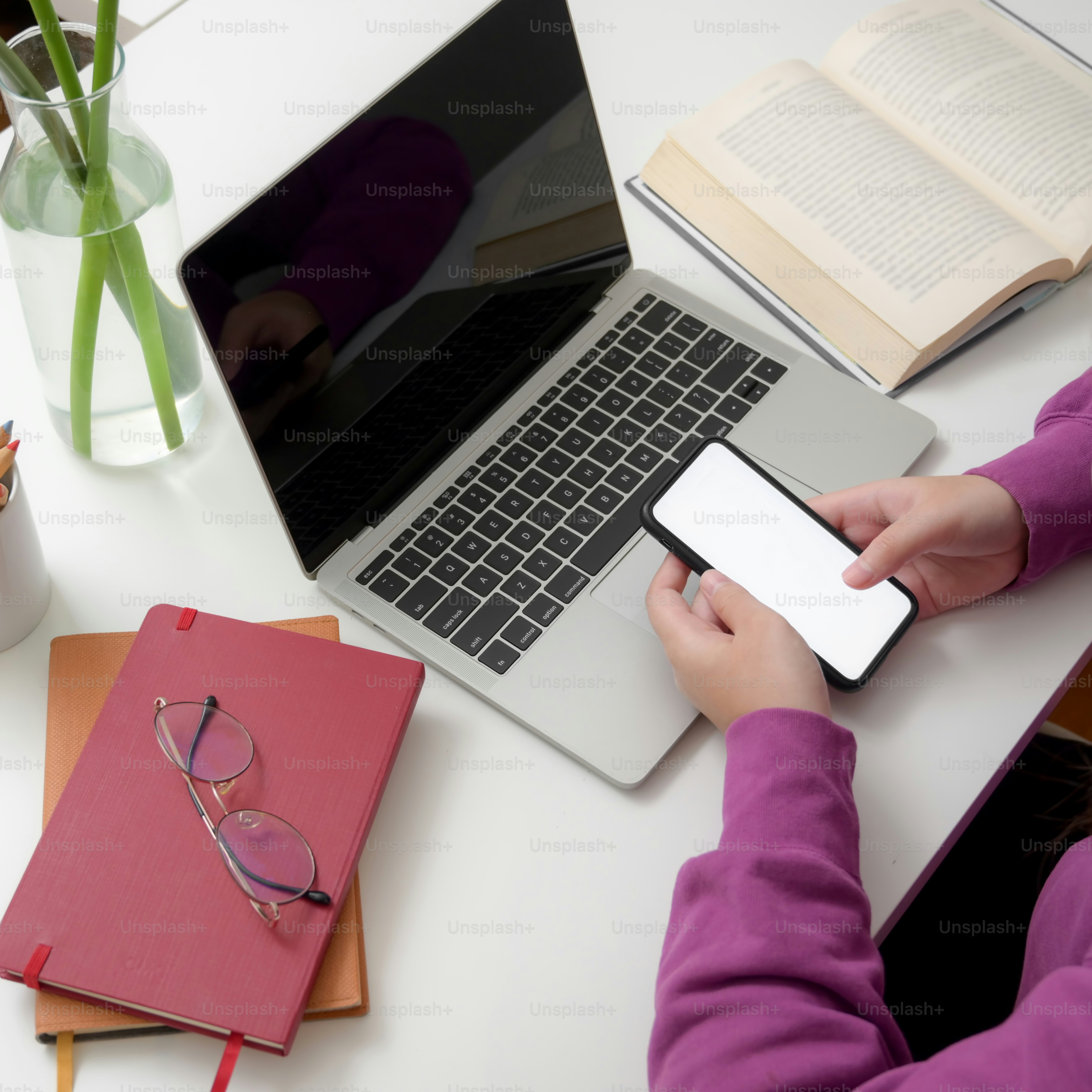 Bidikan di atas kepala gadis perguruan tinggi muda menggunakan smartphone untuk menemukan informasi untuk tesisnya di meja putih dengan laptop dan buku