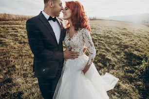happy stylish bride and groom smiling in sunlight, embracing in mountains at sunset light. gorgeous wedding couple newlyweds, true feelings. emotional romantic moment. space for text