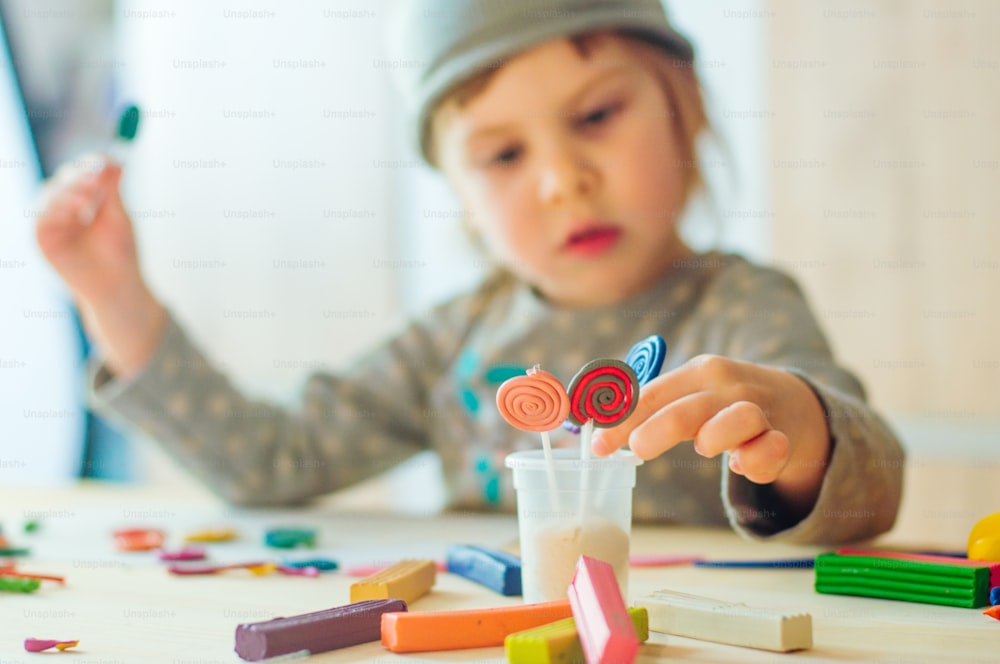 Belle petite fille moulant des sucettes en argile colorées pour les jeux d’enfant sur la table en bois. Mise au point sélective sur les sucettes.