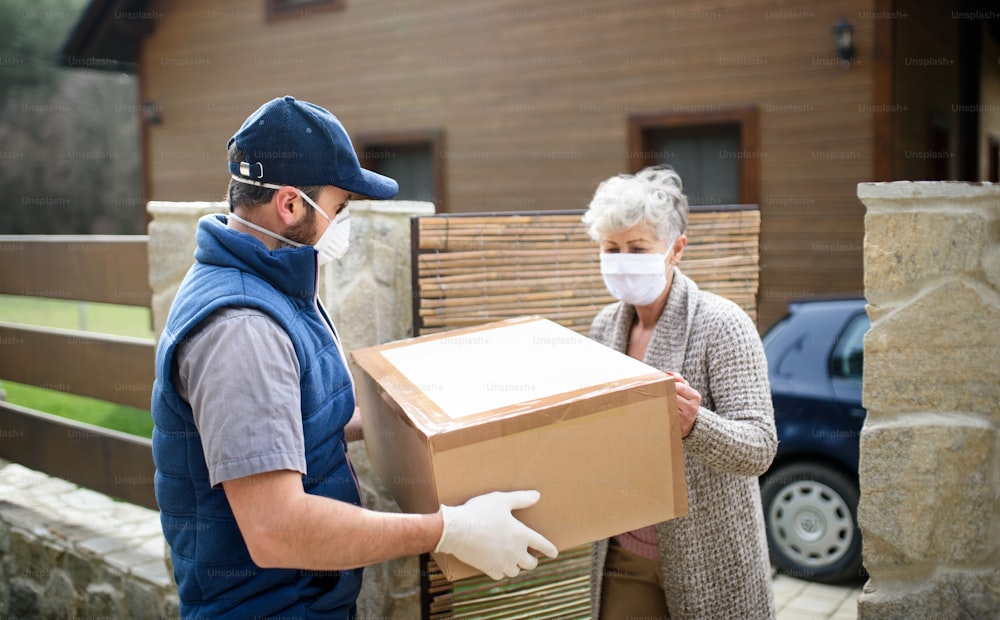 フェイスマスク、コロナウイルス、検疫のコンセプトを持つ年配の女性に小包を配達する男性の宅配便。