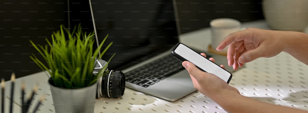 Cropped shot of male photographer looking on mock-up smartphone while sitting at workplace