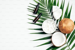 Coconut essential oil with palm leaf and sliced coconut on white background. Flat lay, top view. SPA natural organic cosmetic for skin care, body treatment concept