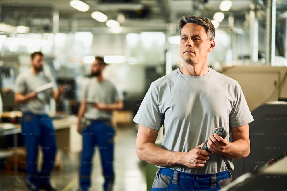 Retrato de un operador CNC adulto medio mirando hacia otro lado mientras está de pie en una fábrica.