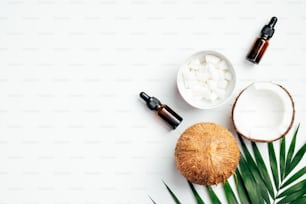 Olio essenziale di cocco naturale per la cura dei capelli con foglia di palma e noci di cocco su sfondo bianco. Concetto di cosmetica, salute e bellezza biologica SPA. Posa piatta, vista dall'alto