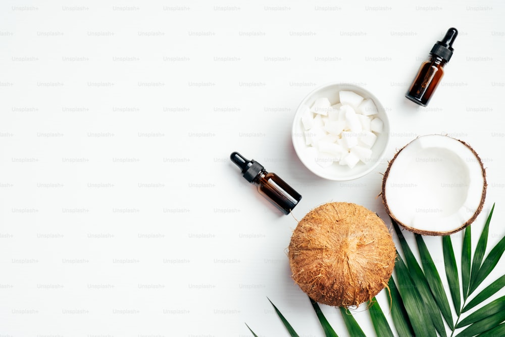 Natural coconut essential oil for hair care with palm leaf and coconuts on white background. SPA organic cosmetic, health and beauty concept. Flat lay, top view
