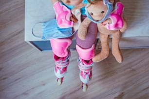 Top view of little girl wearing pink roller skates holding her face mask and bunny soft toy in the mask sitting indoor. Selective focus on the mask. Social distance stay at home during Covid-19 Pandemic concept.