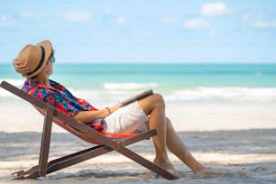 Joven asiático acostado en silla de playa en la playa de la isla tropical en vacaciones de verano