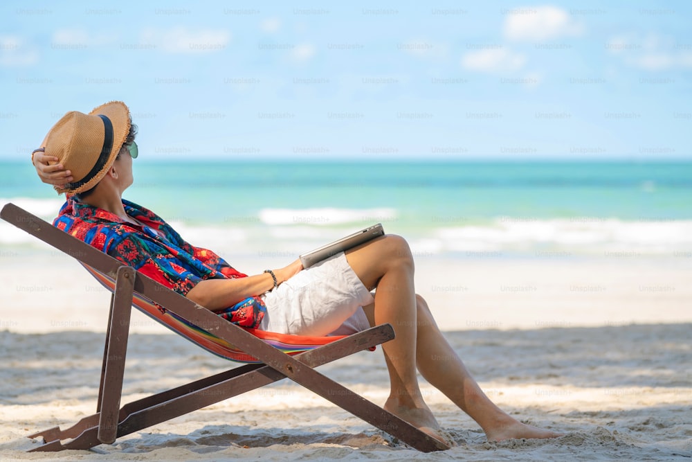 Young Asian man lying on beach chair on tropical island beach in summer vacation