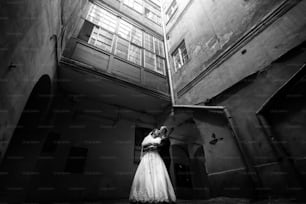 happy gorgeous bride and stylish handsome groom hugging on background of an amazing old building in light, black white