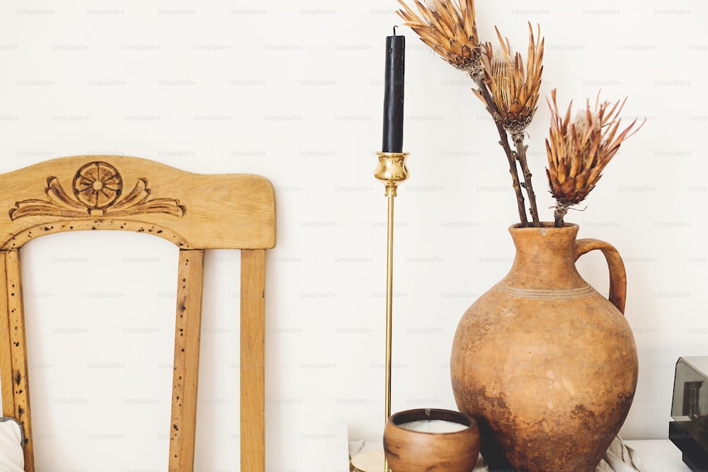 Fiori secchi di protea in un vecchio vaso di argilla e candela sullo sfondo della parete bianca in una casa di campagna. Arredamento moderno della casa. Elementi di interior design semplici ed eleganti. Casa rurale