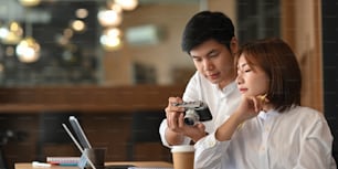 Photo of young couple working together with computer laptop and document while sitting at the wooden working desk over comfortable cafe as background.