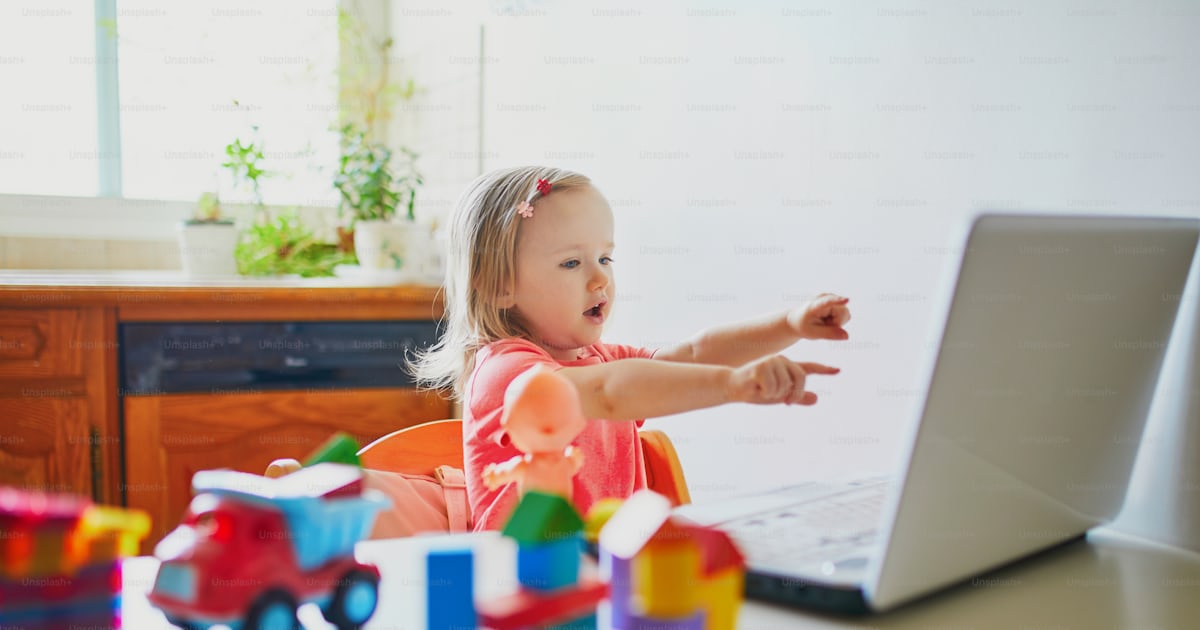 Happy toddler girl with laptop and toys. Kid using computer to ...