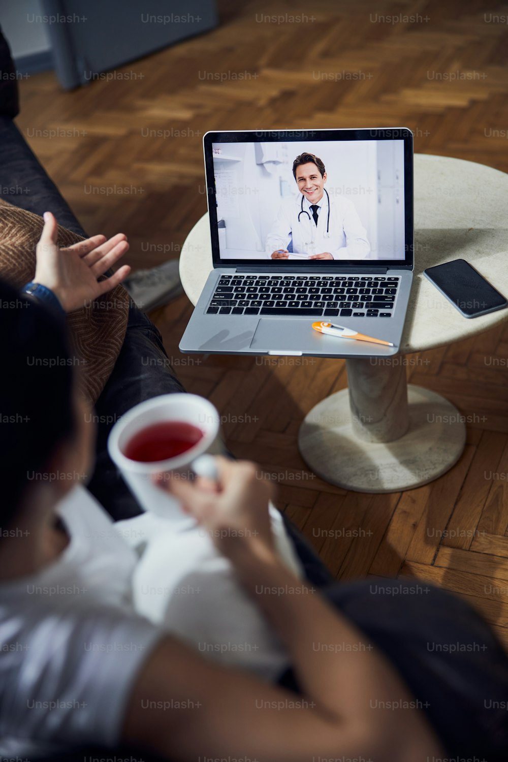 Cropped photo of young lady drinking tea and talking to her doctor online in her flat stock photo. Lifestyle concept