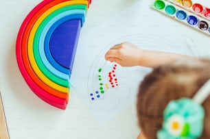 Top view of  little girl painting dot rainbow using cotton sticks on white background. Idea for DIY indoor activities for children.