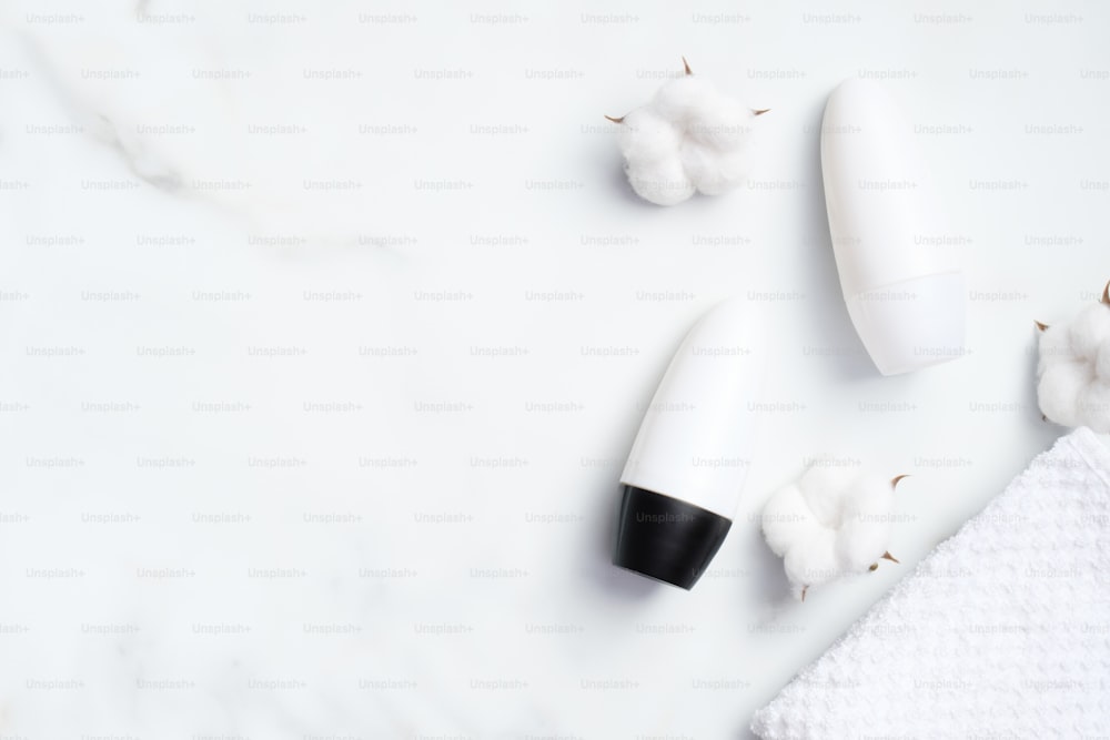 Frascos de desodorante roll-on em branco com algodão e toalha no fundo de mármore. Antitranspirante orgânico natural, conceito de proteção do suor. Flat lay, vista superior