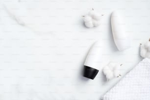 Flacons de déodorant roll-on vierges avec coton et serviette sur fond marbre. Antisudorifique bio naturel, concept de protection contre la transpiration. Pose à plat, vue de dessus